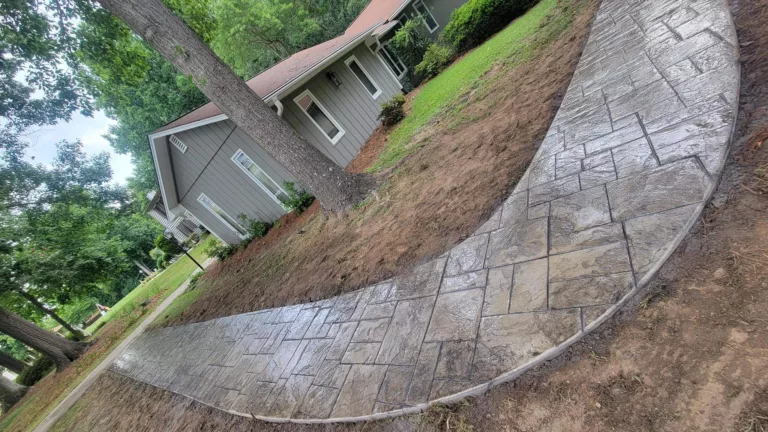 Curved gray stamped concrete patio beside a ranch-style home
