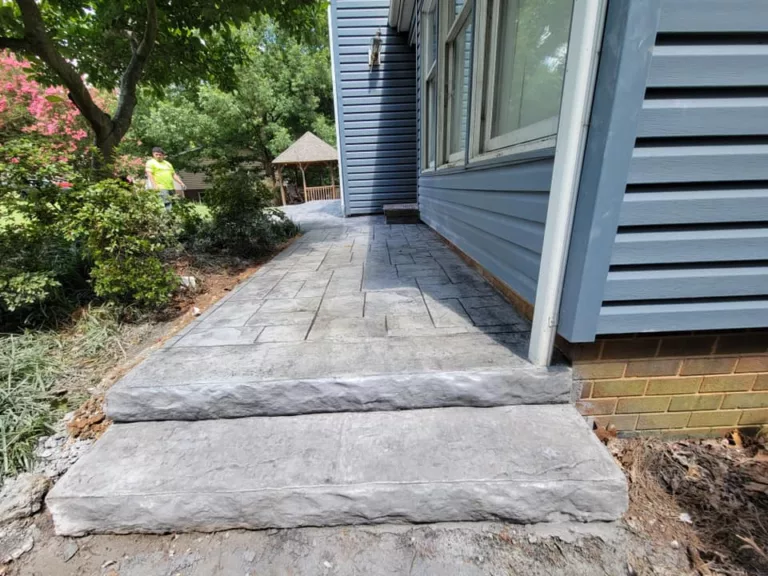 Gray stamped concrete walkway running alongside a blue house