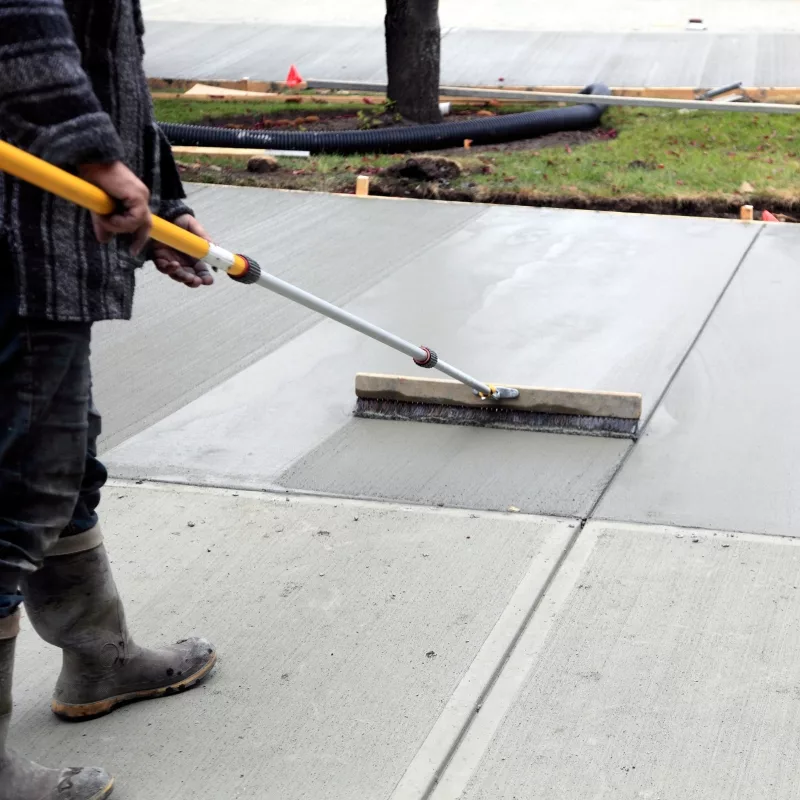 Worker smoothing freshly poured concrete sidewalk surface
